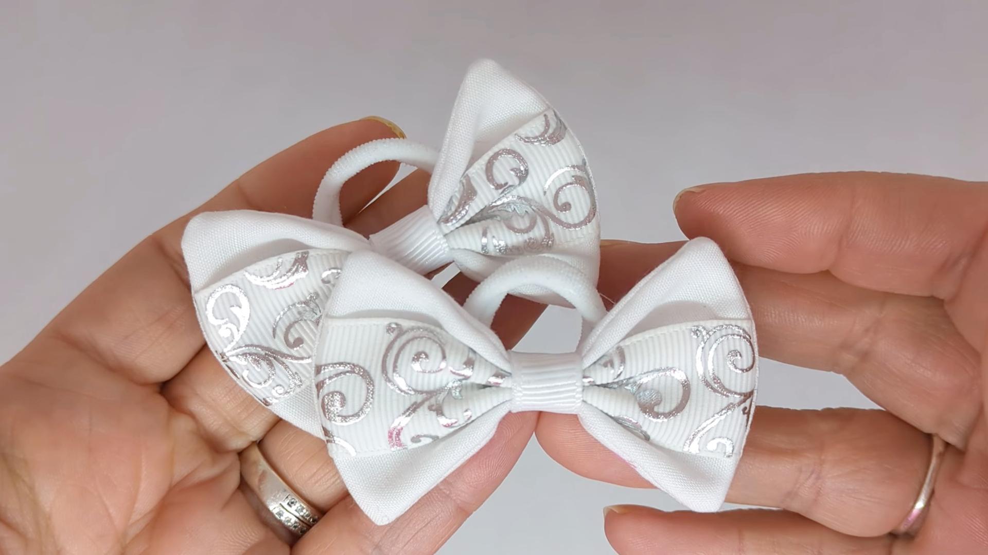 Close-up of white and silver novelty design hair bows on soft polyester bobbles, measuring 6cm x 4cm, showcasing the combination of cotton fabric and grosgrain ribbon.