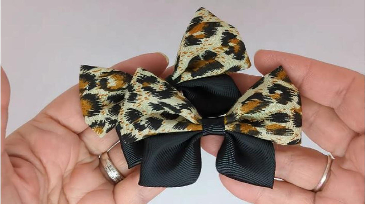 Close-up of black leopard print hair bows on alligator clips, measuring 8cm x 6cm, showcasing the bold leopard pattern and combination of fabric and grosgrain ribbon.