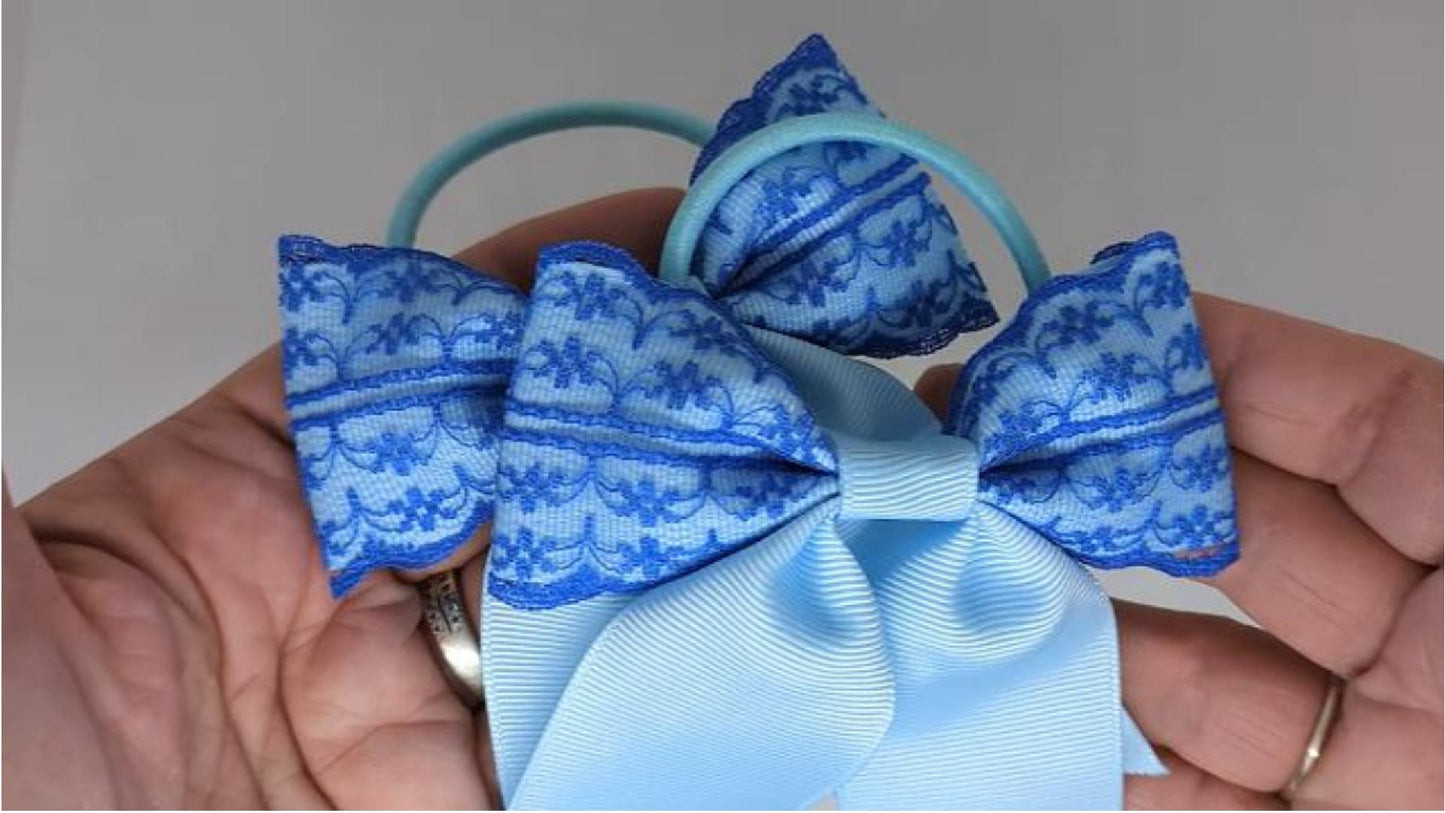 Close-up of baby blue and royal blue lace hair bows on thick bobbles, measuring 10cm x 10cm, showcasing the intricate lace and grosgrain ribbon combination.