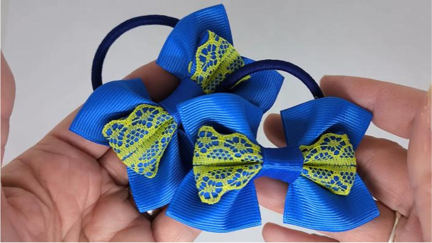 Close-up of royal blue and yellow hair bows on thick bobbles, measuring 9cm x 6cm, showcasing the delicate lace and grosgrain ribbon combination.