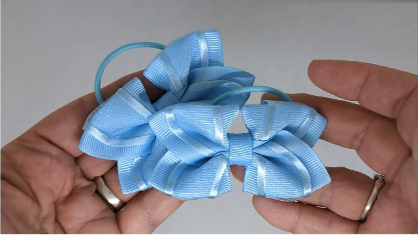 Close-up of baby blue organza hair bows on thin bobbles and snap clips, highlighting the soft organza and grosgrain ribbon texture.