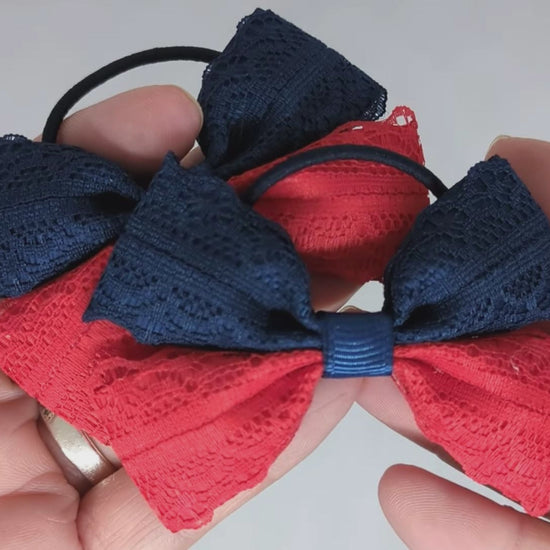 Close-up of navy blue and red school hair bows on thin bobbles, made from grosgrain ribbon and lace, measuring 7cm x 5cm. The bows are displayed to highlight the detailed lace and vibrant colours.